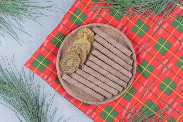 Assiette de kiwi séché et bâton de biscuits sur nappe colorée.