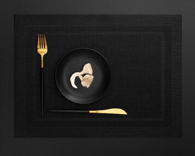 Assiette noire aux champignons sur un drap sombre avec un couteau et une fourchette
