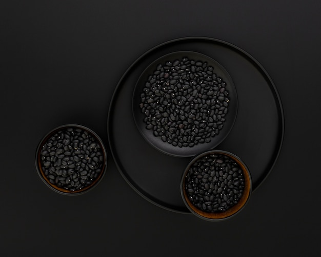 Assiette noire avec des bols noirs de haricots sur fond noir