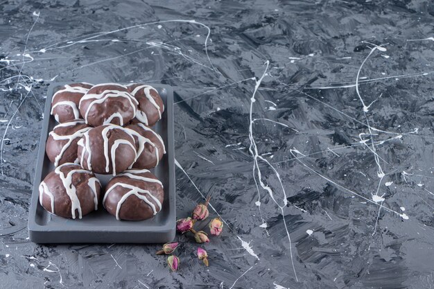 Assiette noire de boules de chocolat avec des roses en herbe sur table en marbre.