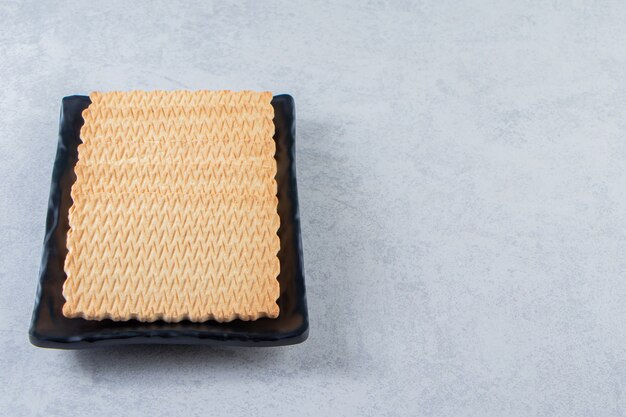 Assiette noire de délicieux biscuits placés sur fond de pierre.