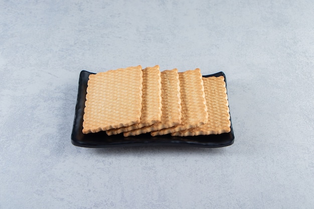 Assiette noire de délicieux biscuits placés sur fond de pierre.