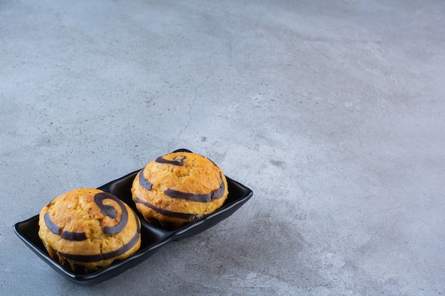 Une assiette noire de deux gâteaux sucrés au sirop de chocolat sur fond gris.