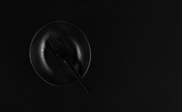 Assiette noire élégante dans le style japonais avec cadre de table à fourche Mise à plat Fond noir Idée de petit-déjeuner minimaliste en couleur noire