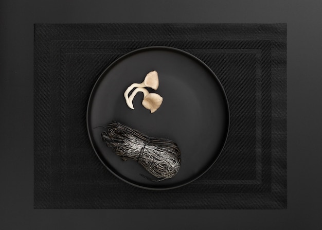 Assiette noire avec des pâtes et des champignons sur un drap noir
