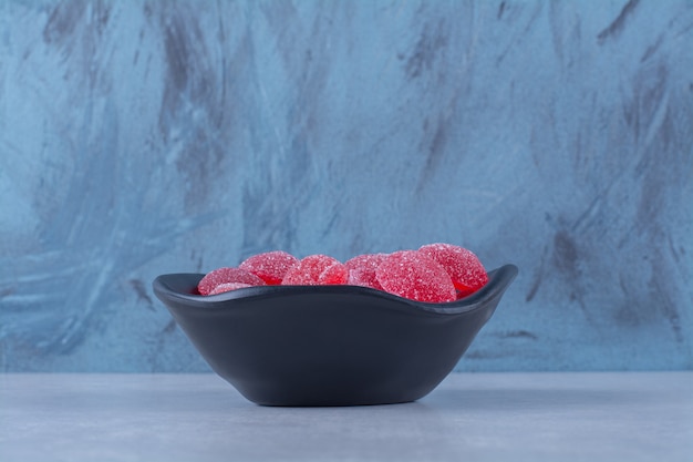 Une assiette noire pleine de bonbons à la gelée de fruits sucrés rouges sur fond gris. photo de haute qualité