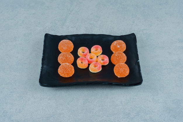 Une assiette noire pleine de bonbons ronds à la gelée d'orange en forme d'anneaux et de bonbons à la gelée d'orange avec du sucre