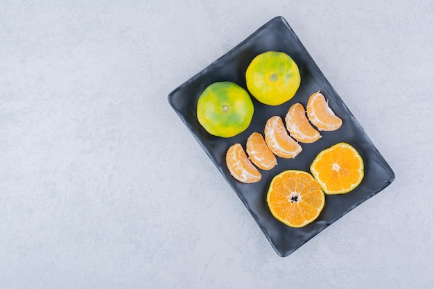 Assiette noire pleine de mandarines aigres sur fond blanc. photo de haute qualité