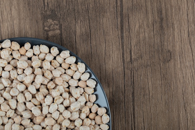 Une assiette noire pleine de pois blancs crus séchés sur table en bois.