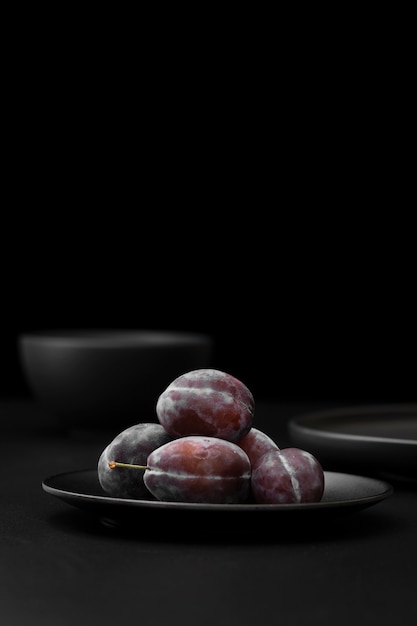 Photo gratuite assiette noire avec des prunes sur une table sombre