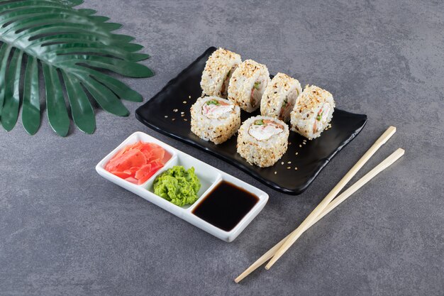Assiette noire de rouleaux de sushi aux graines de sésame sur fond de pierre.