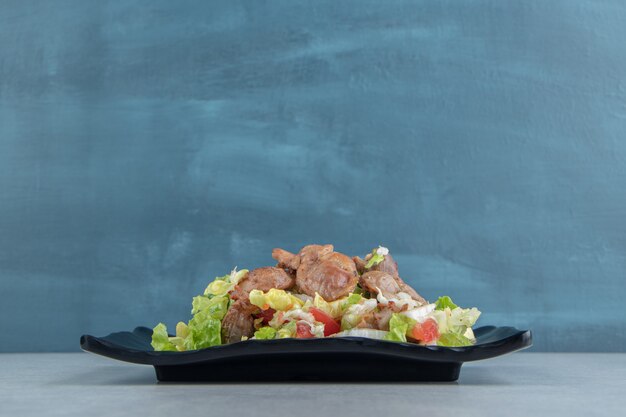 Une assiette noire de viande frite au poulet et salade de légumes.