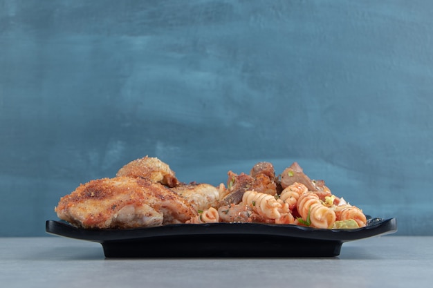 Une assiette noire de viande frite au poulet et salade de légumes.