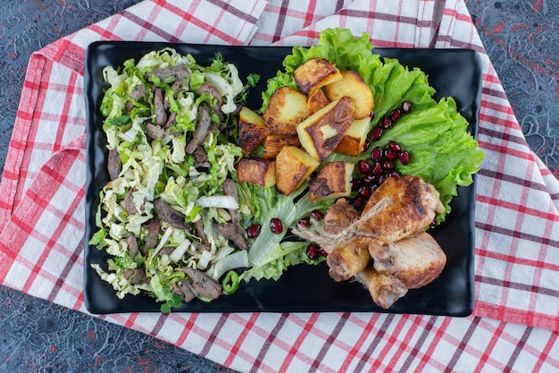 Une assiette noire de viande de poulet avec salade de légumes.