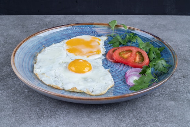 Une assiette avec des œufs au plat et des légumes tranchés. Photo de haute qualité