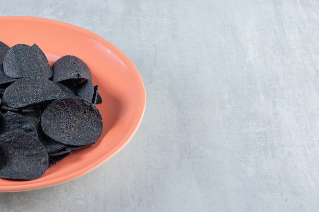 Assiette orange de chips noires croustillantes sur pierre.