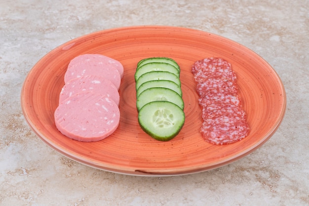 Assiette orange de délicieuses saucisses fumées et tranchées sur une surface en marbre.