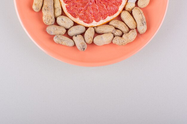 Assiette orange de tranche de pamplemousse et cacahuètes biologiques sur fond blanc. photo de haute qualité