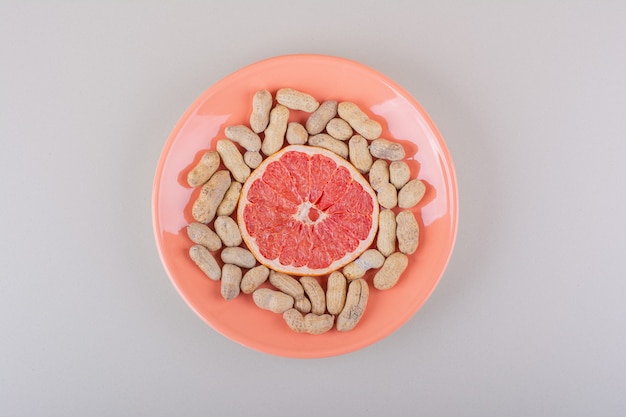 Assiette Orange De Tranche De Pamplemousse Et Cacahuètes Biologiques Sur Fond Blanc. Photo De Haute Qualité