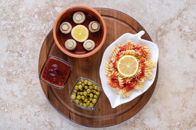 Assiette de pâtes cuites avec diverses portions de garniture sur un plateau en bois sur une surface en marbre