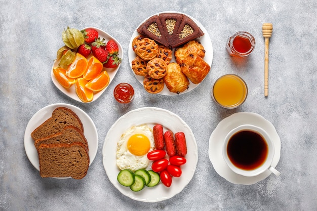 Une assiette de petit-déjeuner contenant des saucisses à cocktail, des œufs au plat, des tomates cerises, des bonbons, des fruits et un verre de jus de pêche.