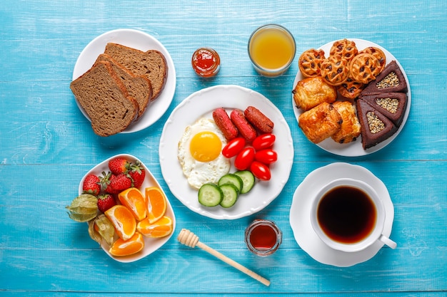 Une assiette de petit-déjeuner contenant des saucisses à cocktail, des œufs au plat, des tomates cerises, des bonbons, des fruits et un verre de jus de pêche.