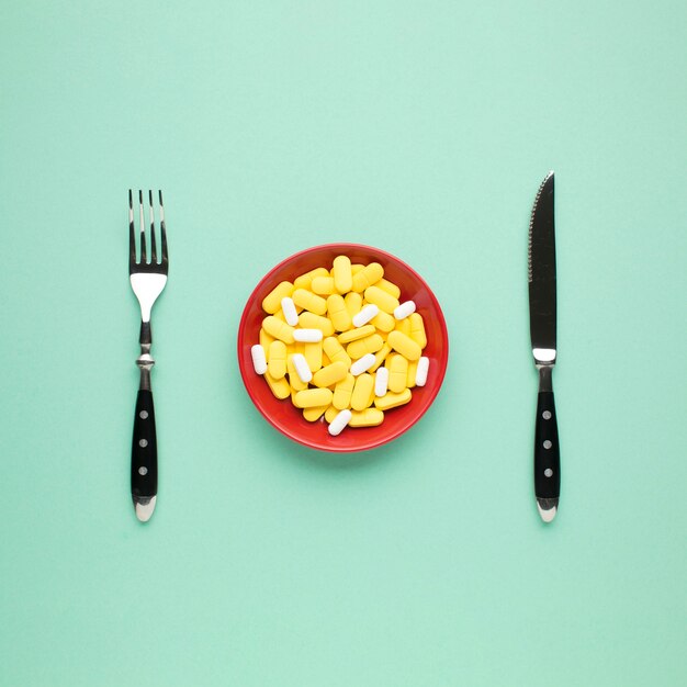 Assiette de pilules jaunes et blanches avec des couverts sur fond vert