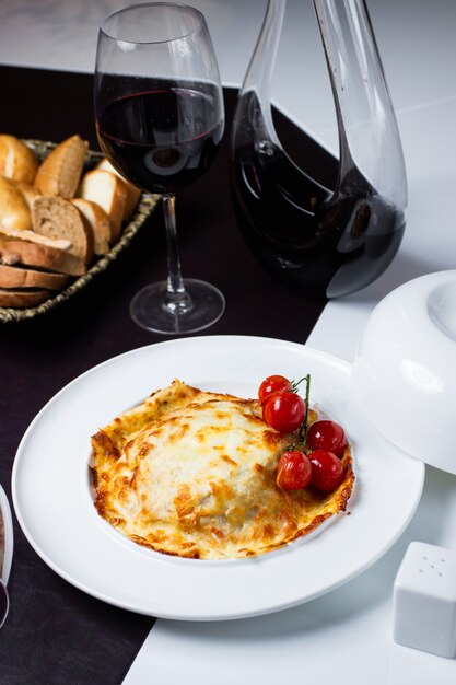 Une assiette de plat recouvert de fromage fondu garni de tomates cerises