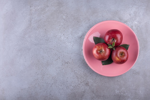 Photo gratuite assiette rose de pommes rouges mûres posées sur pierre.