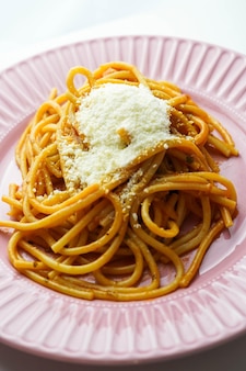 Une assiette rose de spaghettis frais à la sauce tomate et au parmesan