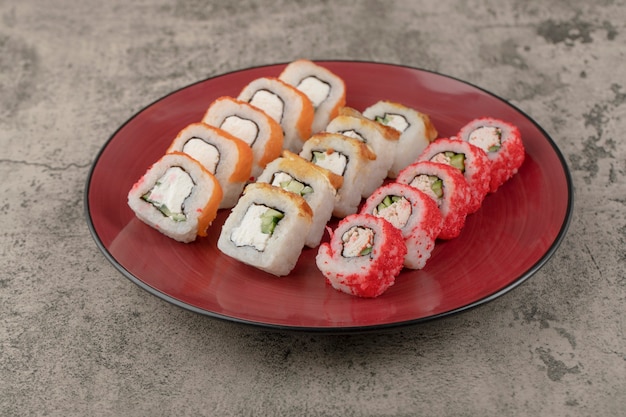 Assiette rouge de divers délicieux rouleaux de sushi sur fond de marbre