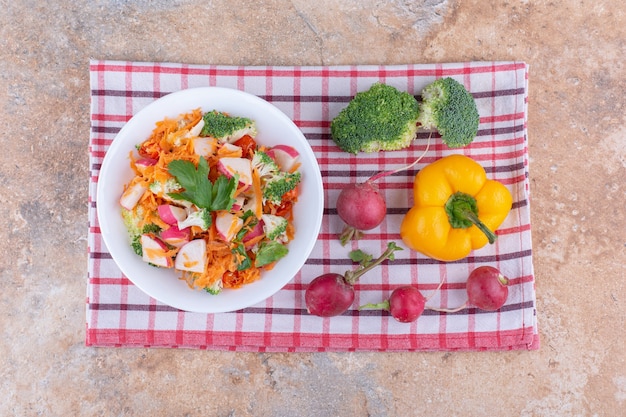 Assiette de salade mixte à côté de divers légumes sur une serviette sur une surface en marbre