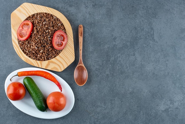 Assiette de sarrasin cuit avec des tranches de tomate à côté d'une cuillère et une assiette de tomate