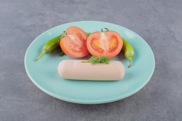 Une assiette avec des saucisses bouillies et des tranches de tomate rouge.