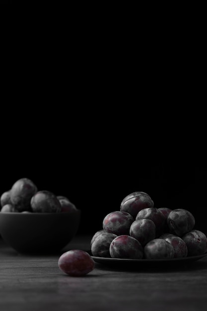 Assiette sombre et bol avec des prunes sur un fond sombre