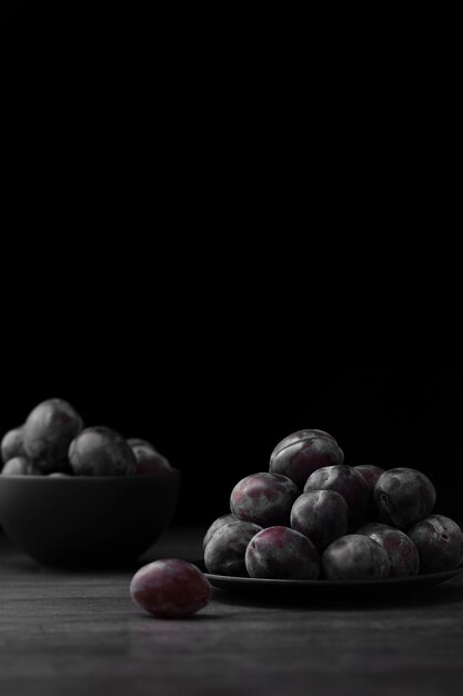 Assiette sombre et bol avec des prunes sur un fond sombre