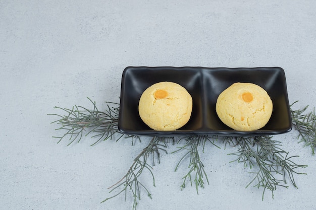 Une assiette sombre avec deux biscuits sucrés ronds sur une surface blanche