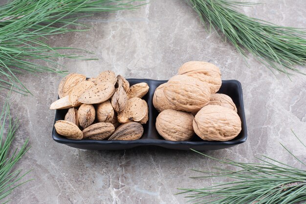 Assiette sombre pleine d'amandes et de noix sur fond de marbre.