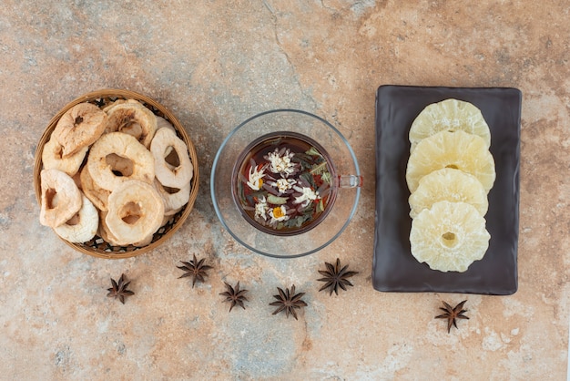 Une assiette sombre pleine d'ananas séché et une tasse de tisane