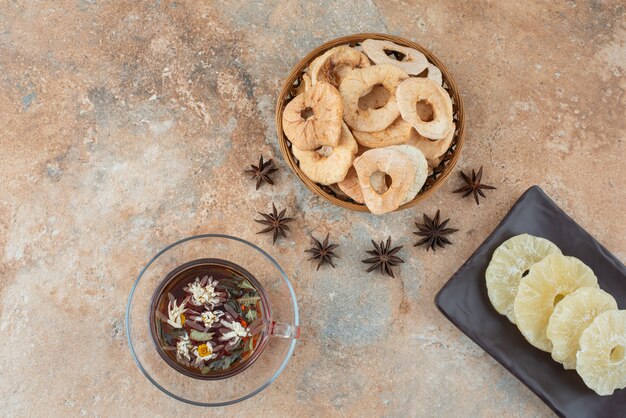 Une assiette sombre pleine d'ananas séché et une tasse de tisane