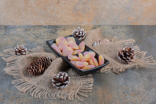 Une assiette sombre pleine de bonbons à la gelée de fruits en forme de cœur et de pommes de pin. Photo de haute qualité