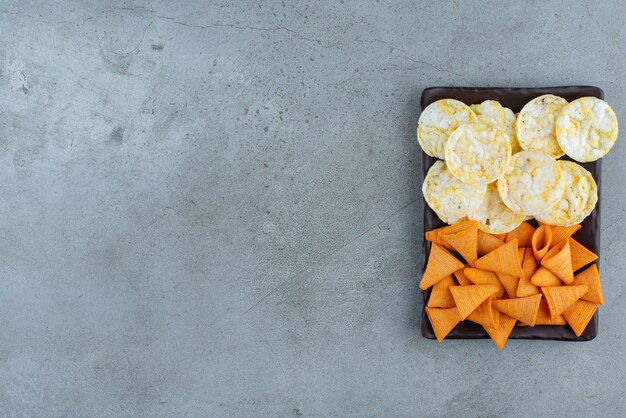 Une assiette sombre pleine de chips croustillantes sur fond gris. photo de haute qualité