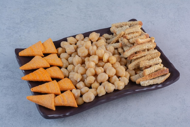 Photo gratuite une assiette sombre pleine de chips jaunes, de gressins et de petits pois