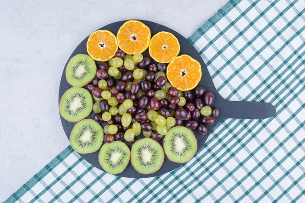 Une assiette sombre pleine de raisins, de kiwi et d'orange sur une nappe. photo de haute qualité
