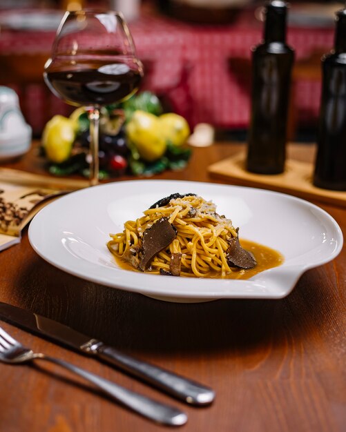 Assiette de spaghetti aux truffes avec sauce aux champignons et parmesan râpé servi avec du vin rouge