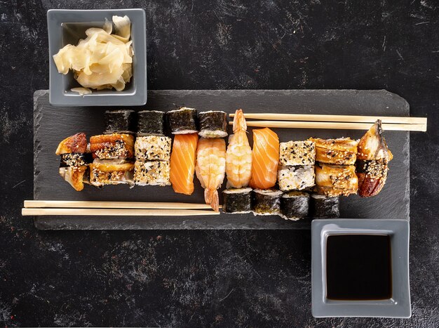 Assiette de sushi sur pierre sombre à côté de baguettes sur fond noir en studio. Cuisine asiatique saine