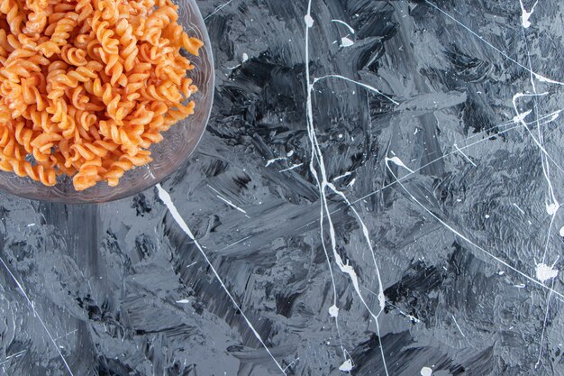 Assiette en verre de délicieuses pâtes fusilli placées sur fond de marbre.