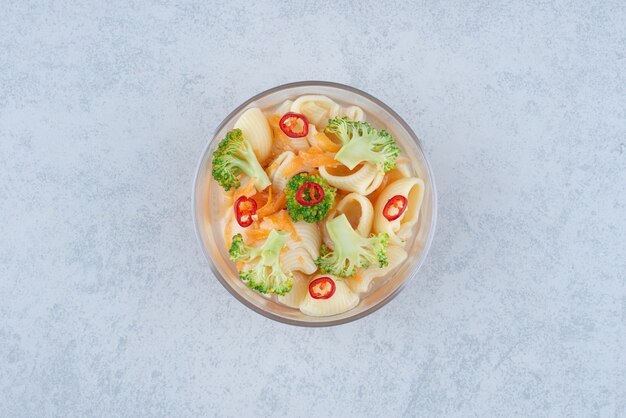 Une assiette en verre de macaroni et brocoli sur surface blanche