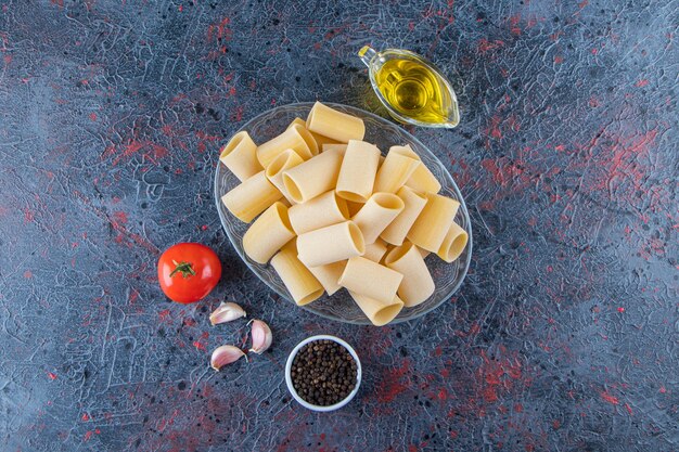 Une assiette en verre de pâtes cannelloni crues à l'ail et à l'huile sur une surface sombre.