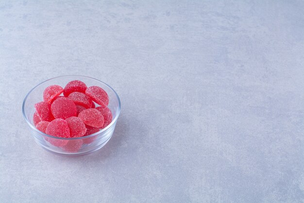 Une assiette en verre pleine de bonbons à la gelée sucrée sur une table grise .